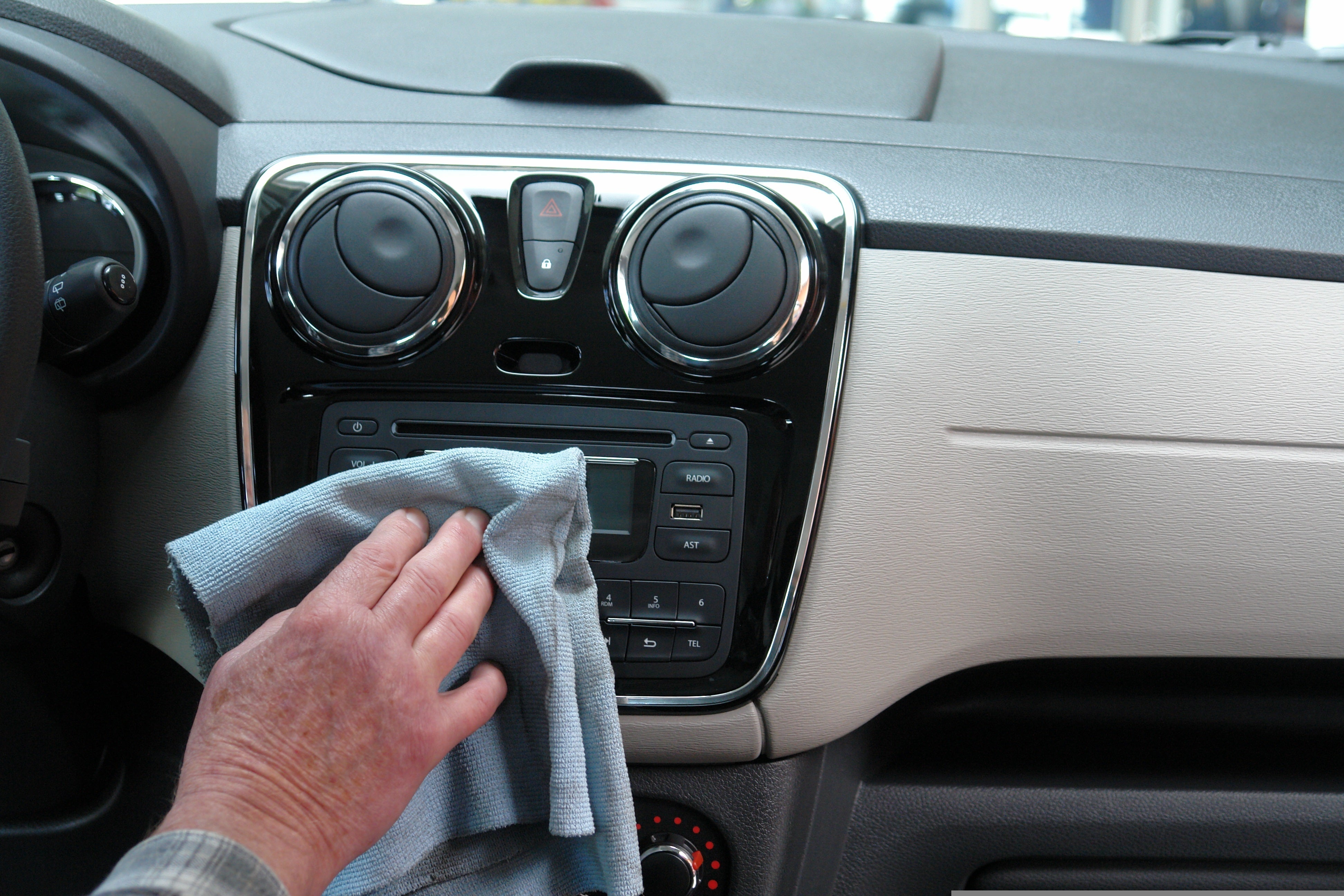 Person wiping the interior of a car, cleaning the dashboard and surfaces for a spotless, well-maintained vehicle.