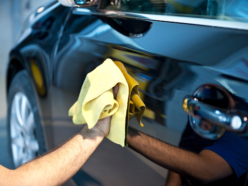 A person wipes down a car with a microfiber cloth, ensuring a scratch-free, streak-free finish to protect the paint and enhance its shine.