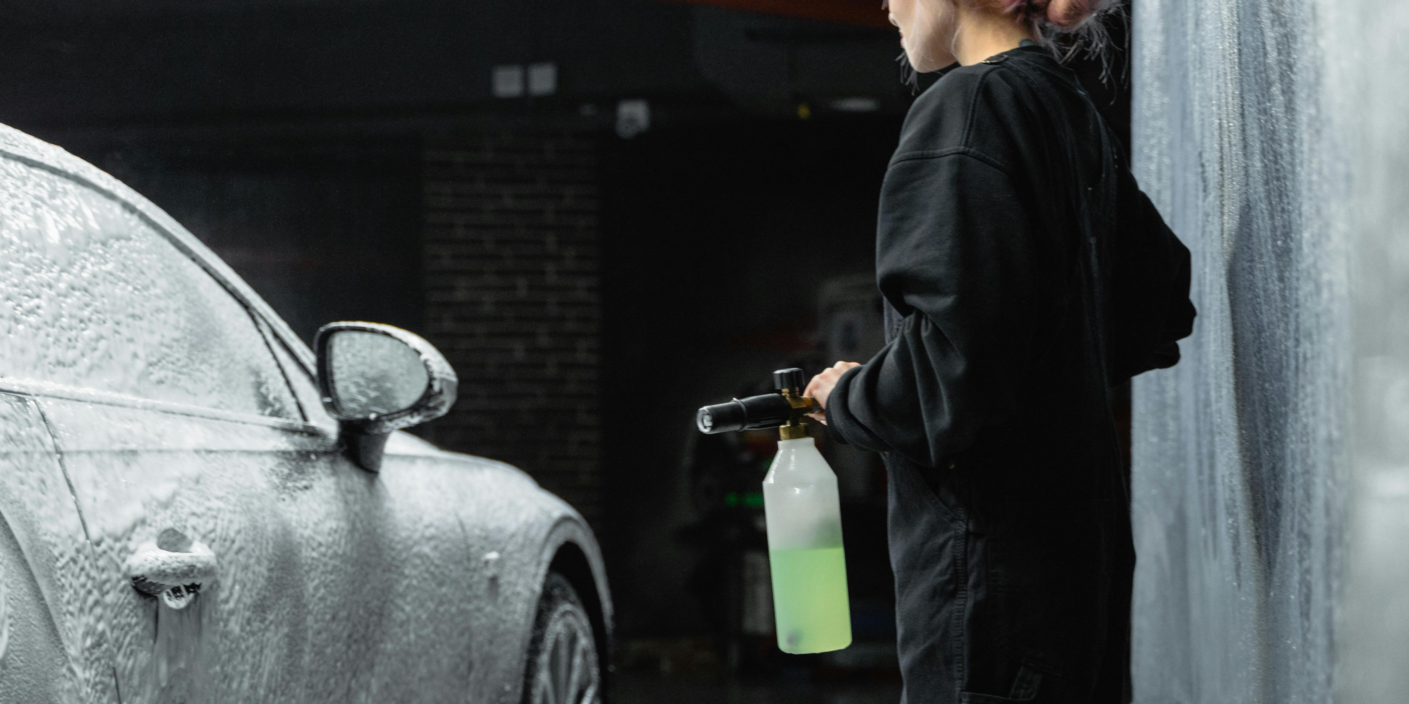 Person washing a car with a pressure sprayer, demonstrating car detailing techniques for beginners.